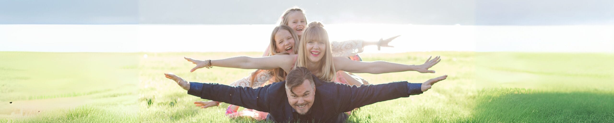 Family stacked on each other's backs with arms spread wide in a sunny field