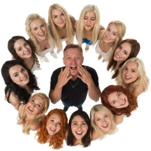 A man at the center surrounded by a circle of smiling women, photographed from above.