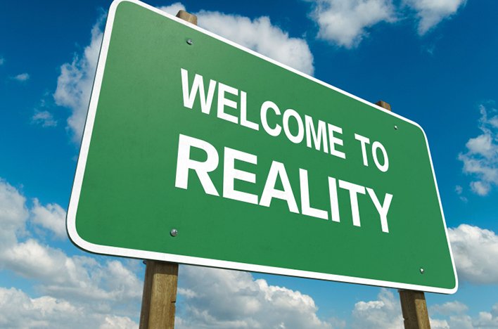 Green road sign reading 'Welcome to Reality' against a blue sky with clouds.