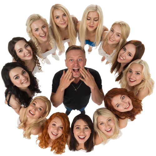 A man at the center surrounded by a circle of smiling women, photographed from above.