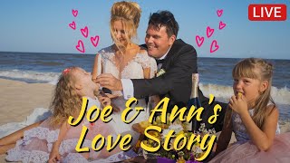 A man and woman in wedding attire sit with two young girls on a sunny beach, toasting with drinks; bold text reads 'Joe & Ann's Love Story' and a LIVE badge.